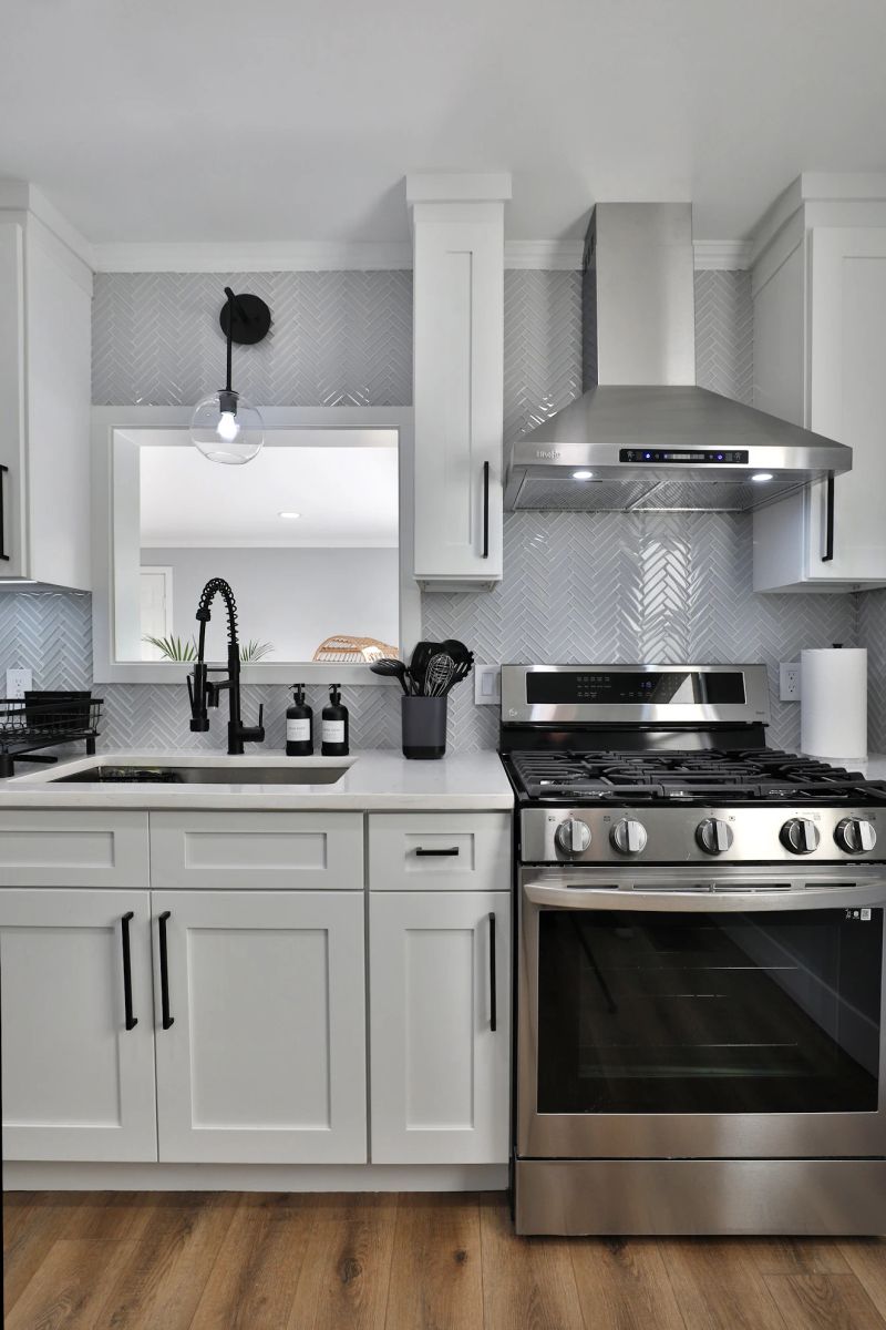 White kitchen sink, range, hood, and herringbone backsplash.