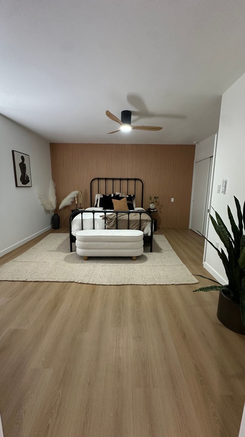 Finished bedroom with light wood flooring, a textured accent wall, and a black metal bed frame.