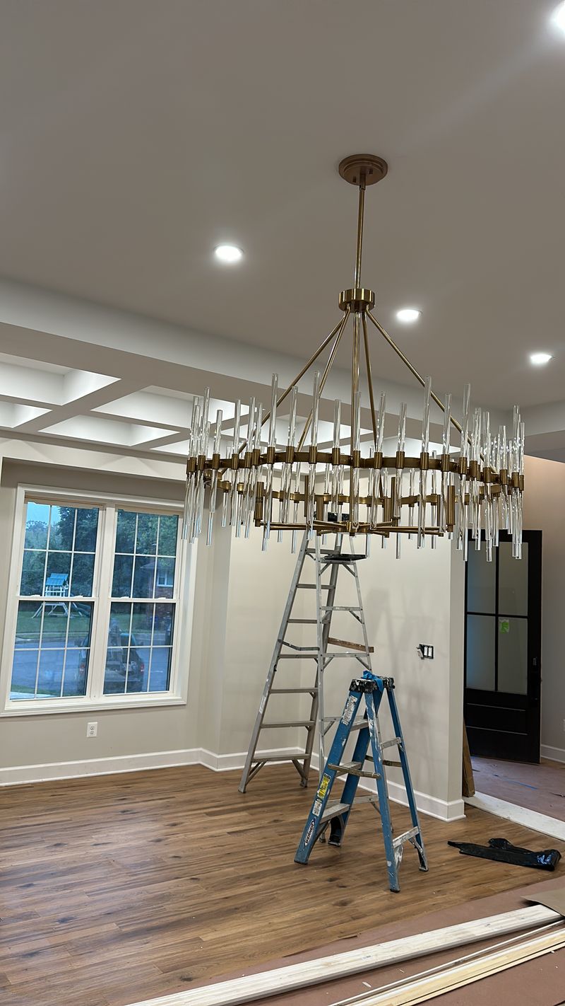 Dining room during renovation with a chandelier, ladder, and unfinished trim
