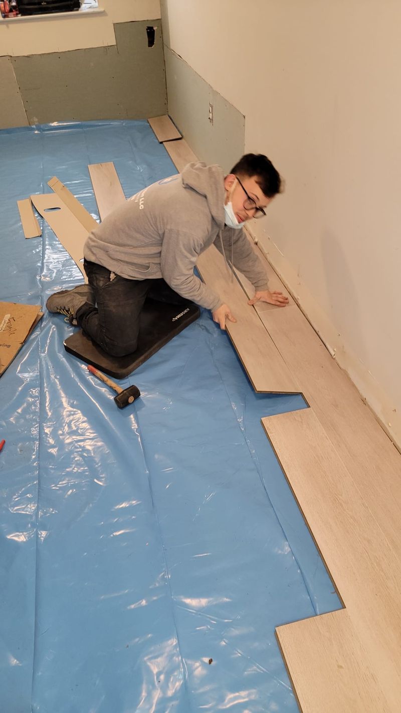 Flooring installation in progress with a worker fitting wood planks over blue underlayment