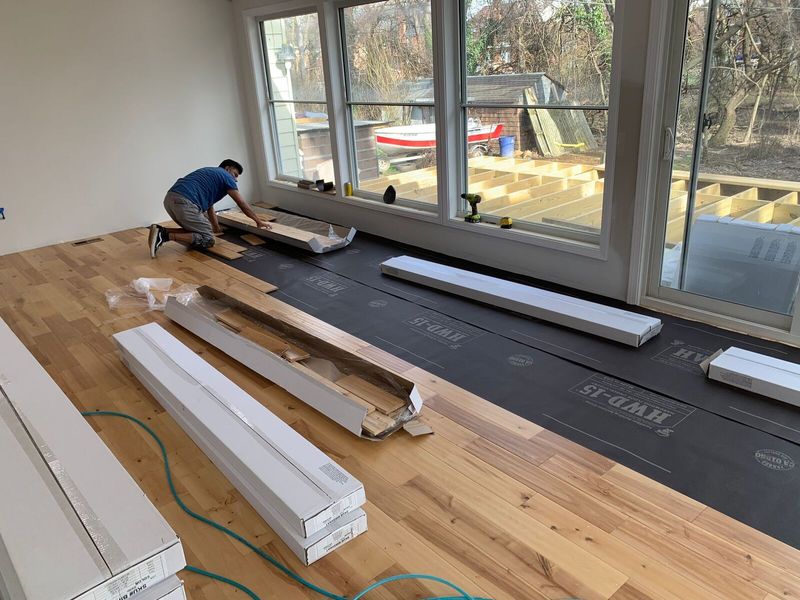 Engineered wood planks being laid over underlayment in front of a window