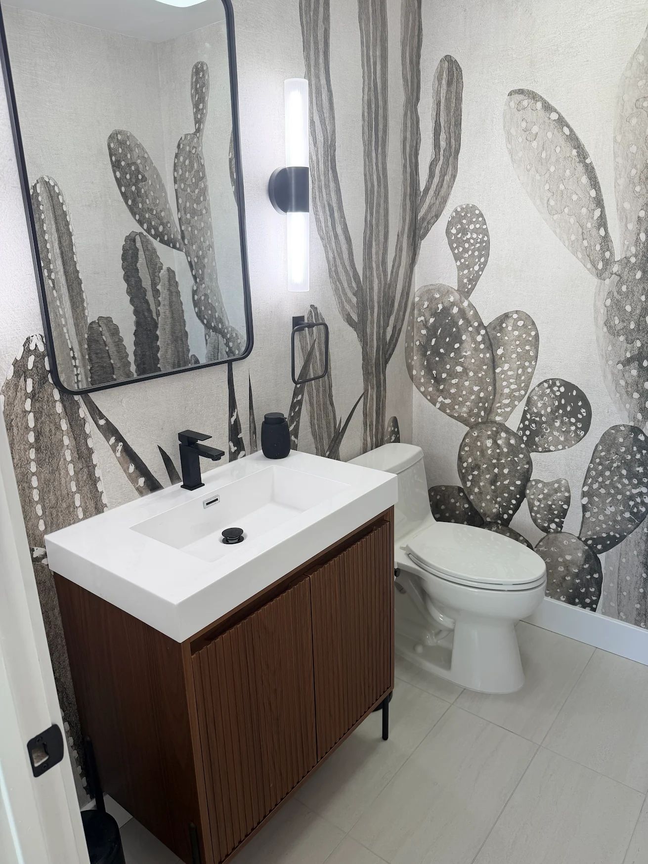 Finished powder room with a fluted walnut vanity, matte black fixtures and a full height cactus mural.