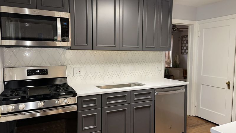 Finished kitchen with charcoal shaker cabinets, gold hardware and white chevron backsplash
