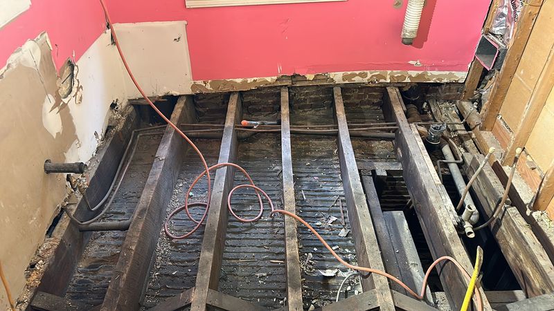 Exposed floor joists reveal the original plumbing beneath the bathroom.