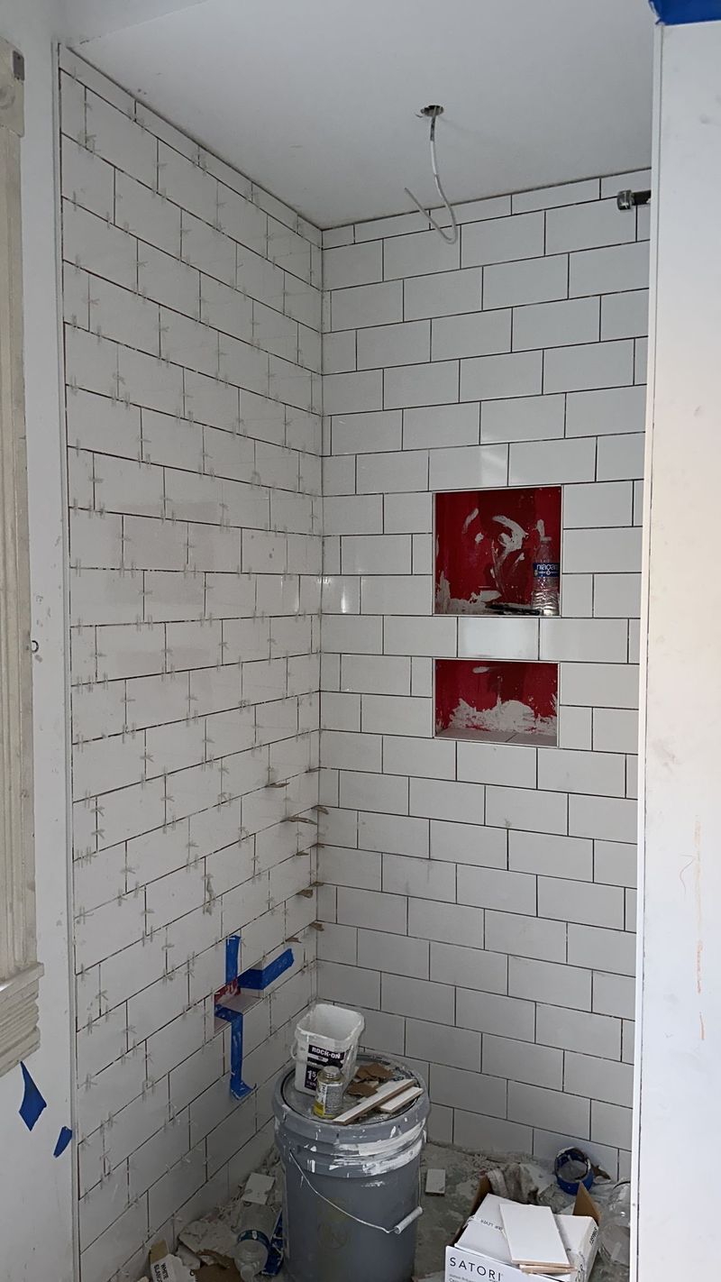 White subway tile installation in progress with spacers, leveling clips, and two unfinished niches.