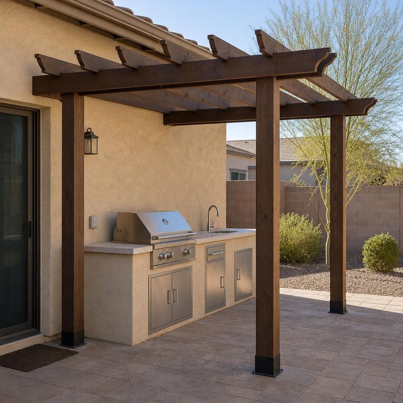 Design concept of a modest outdoor kitchen with a stainless steel grill and sink beneath a wood pergola.