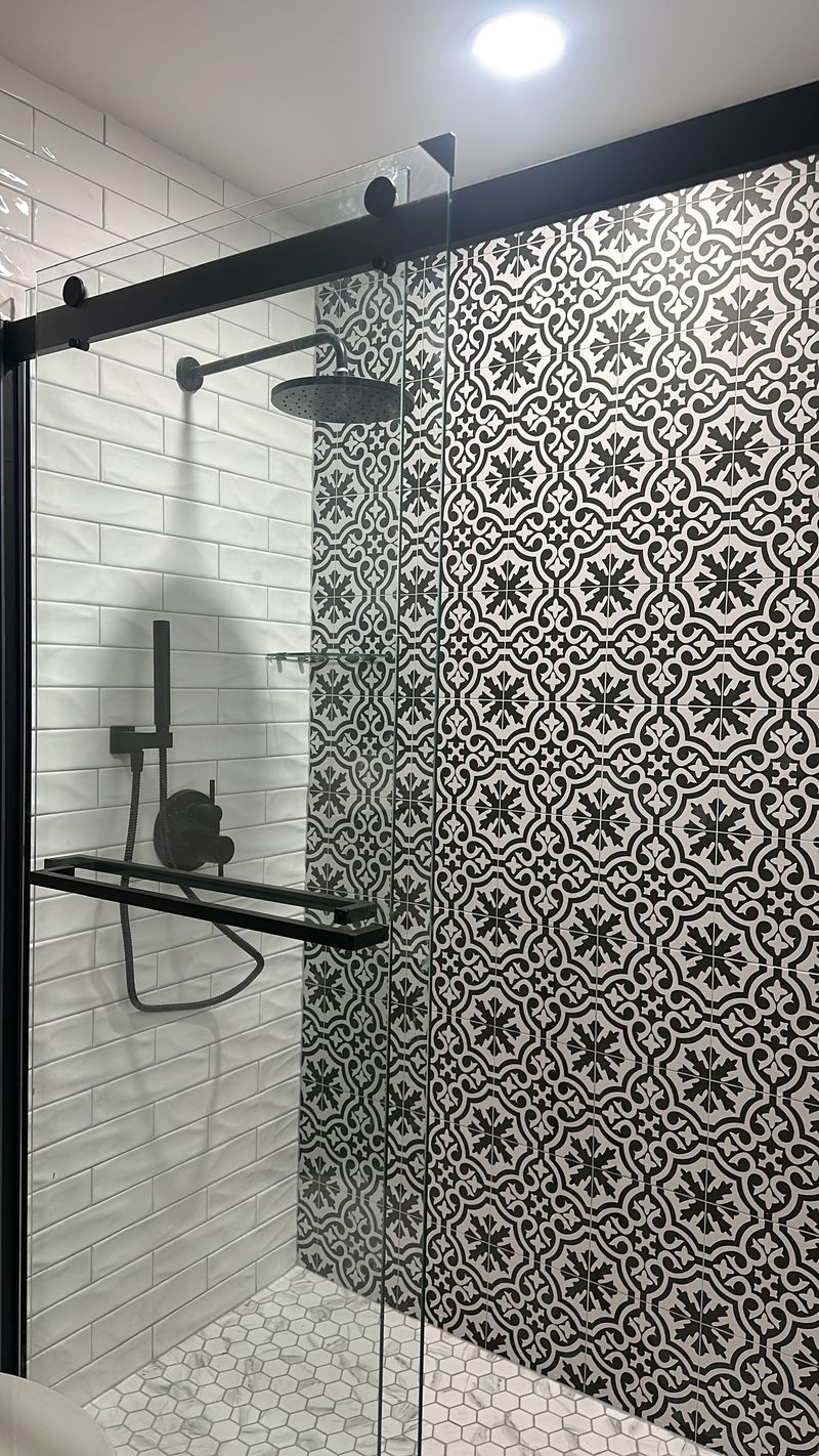 Patterned black-and-white tile shower wall with matte black rain head and handheld shower.