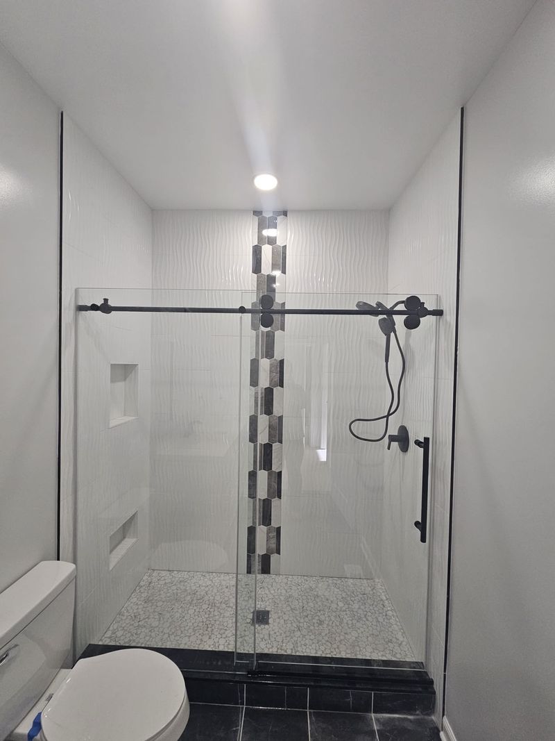 White wave-tile walk-in shower with hexagon accent strip, two niches and black hardware.