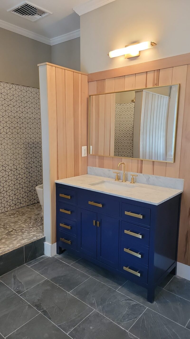 Blue bathroom vanity beneath a mirror on a wood paneled wall