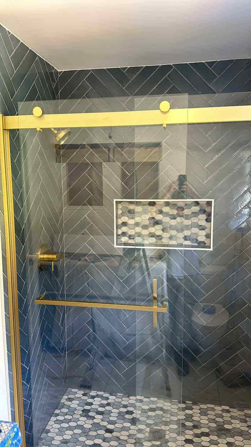 Dark herringbone shower tile with warm metal fixtures