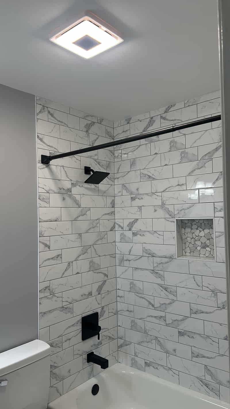 Tub surround with marble look subway tile and matte black fixtures