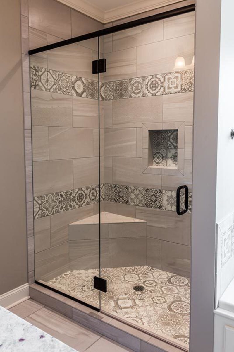 Glass enclosed walk in shower with patterned tile bands, a niche, and a corner bench