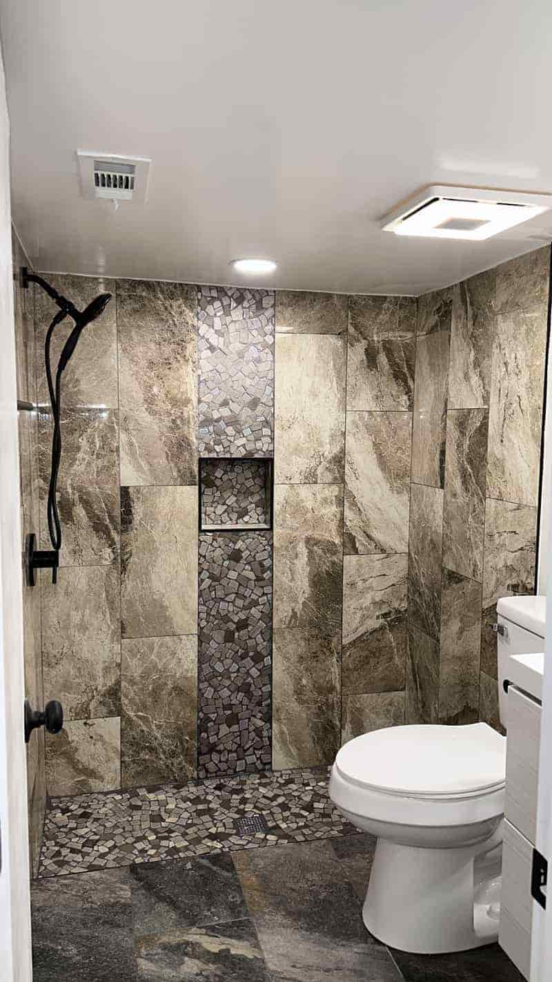 Walk in shower with stone tile and a vertical mosaic detail