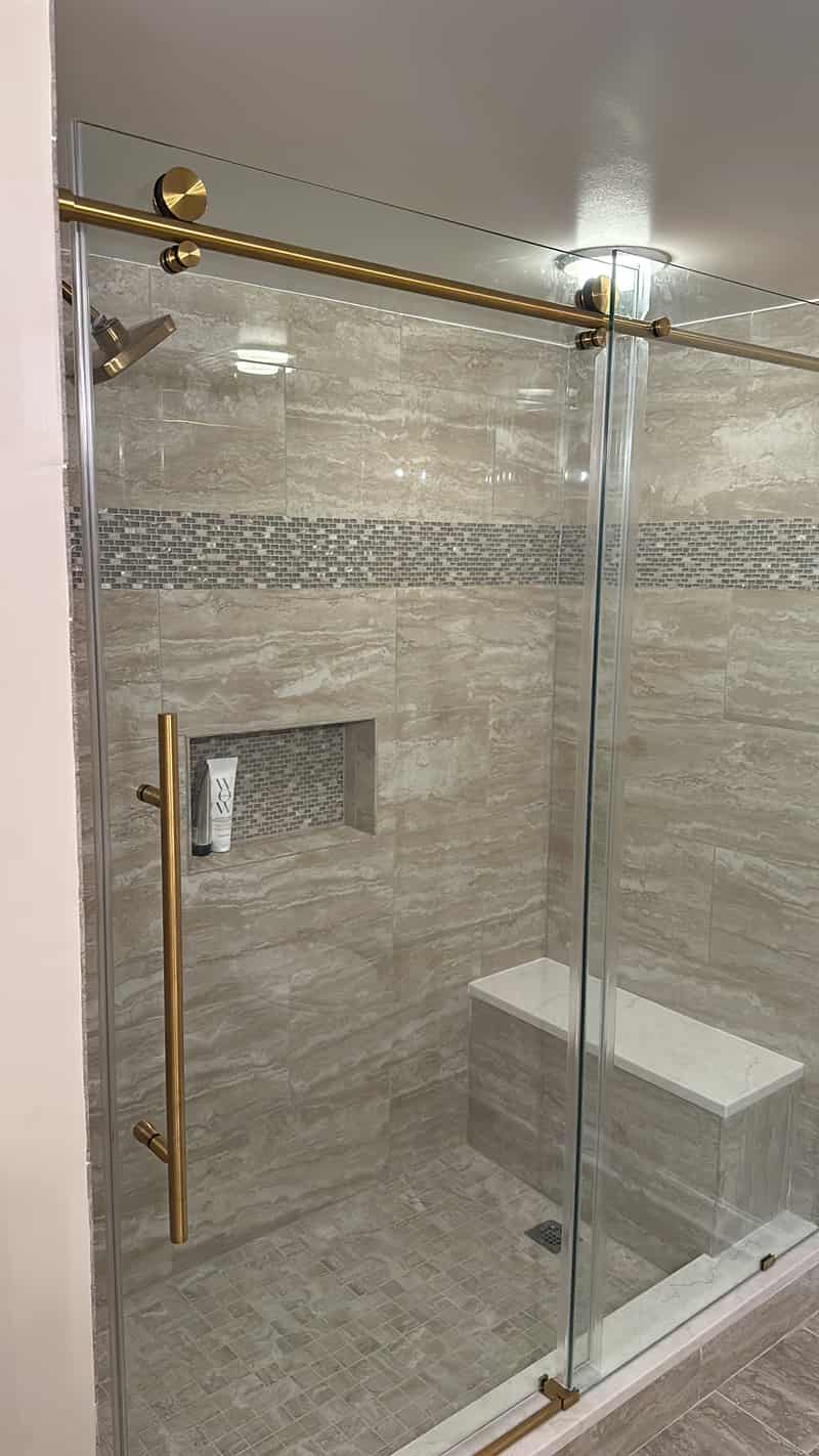 Gray tiled shower with brass hardware, a built in bench, and a niche